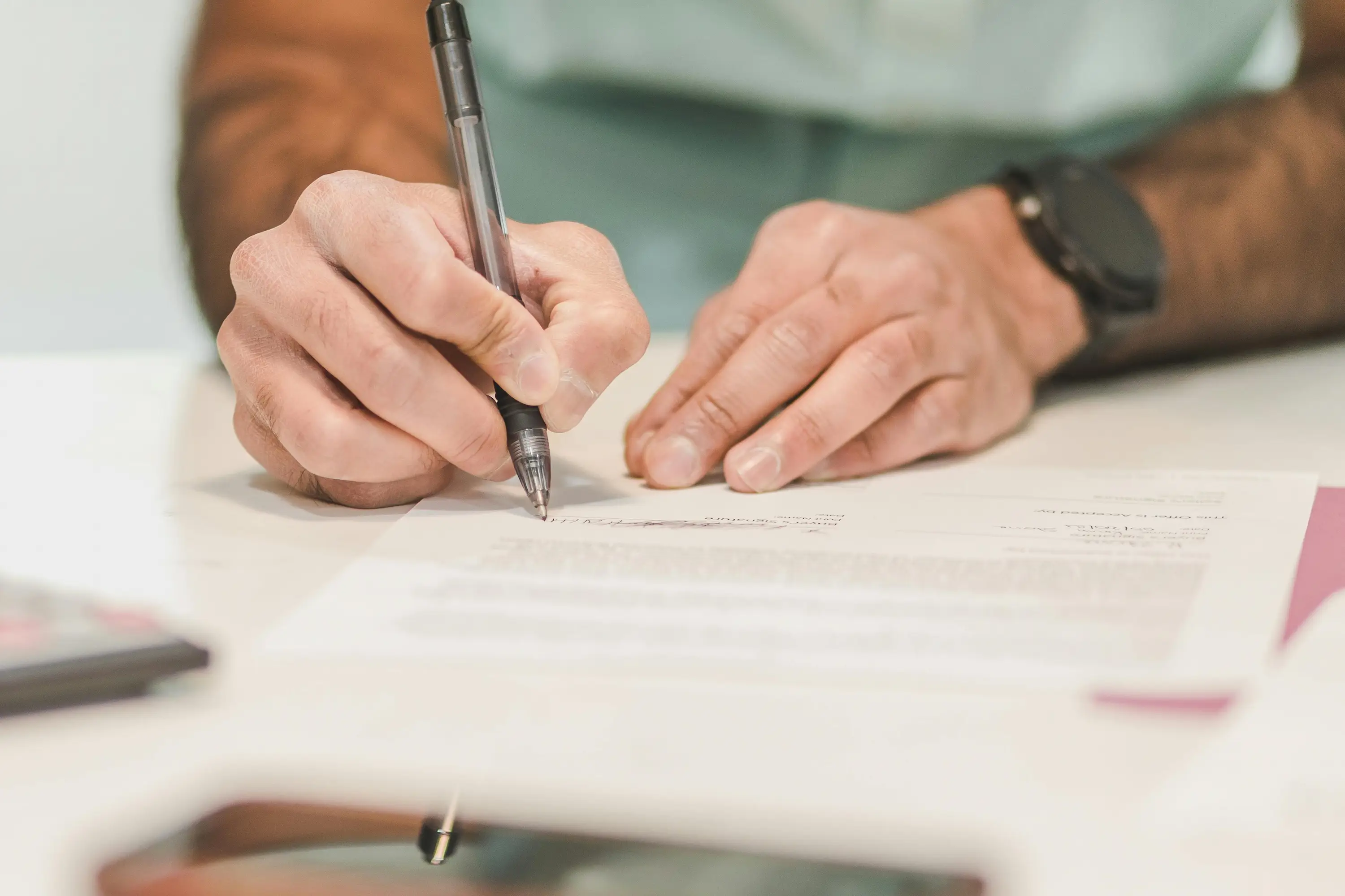 Une personne tenant un stylo et signant un document officiel sur une table blanche.