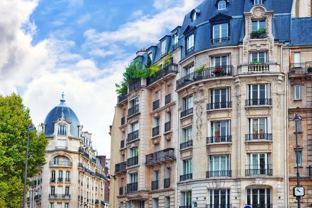Façades d'immeubles haussmanniens avec toits en ardoise et balcons en fer forgé sous un ciel bleu.