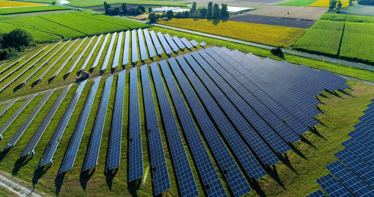 Vue aérienne d'un grand champ de panneaux solaires alignés avec des champs agricoles autour.