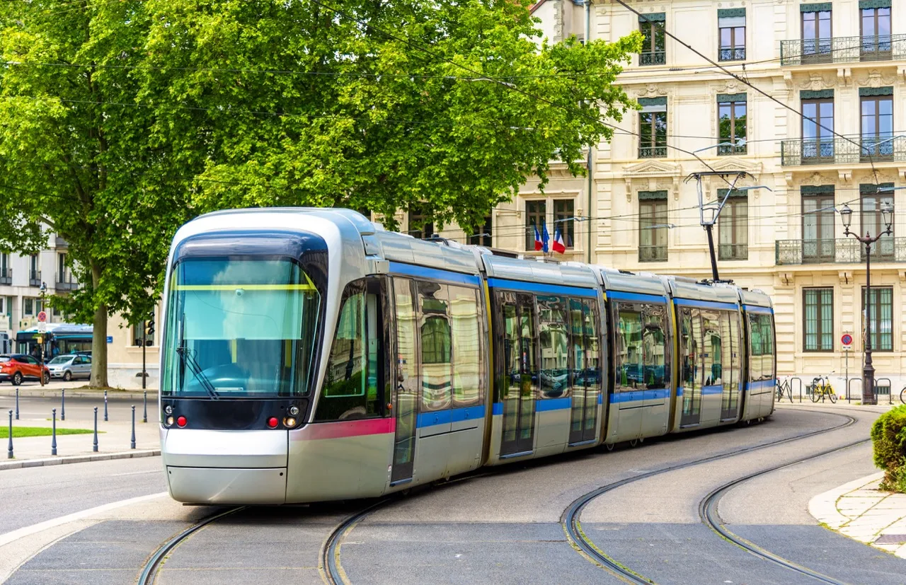 Tramway moderne circulant sur une voie sinueuse en ville avec des bâtiments et des arbres en arrière-plan.