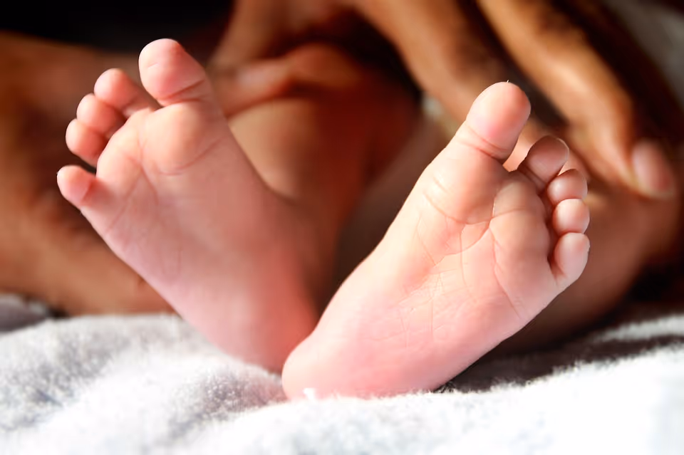 Close-up of baby feet resting on a soft white surface with adult hands gently holding them.