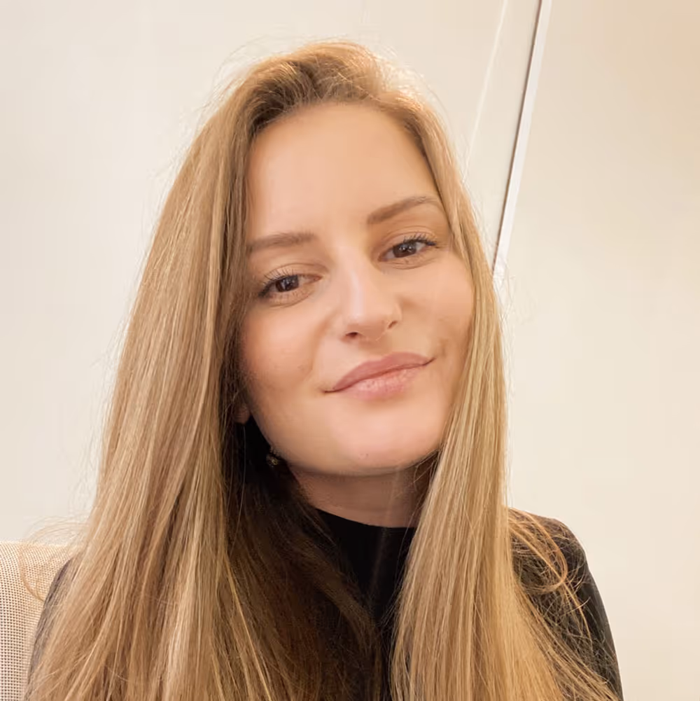 Close-up of a woman with long light brown hair smiling gently against a light background.