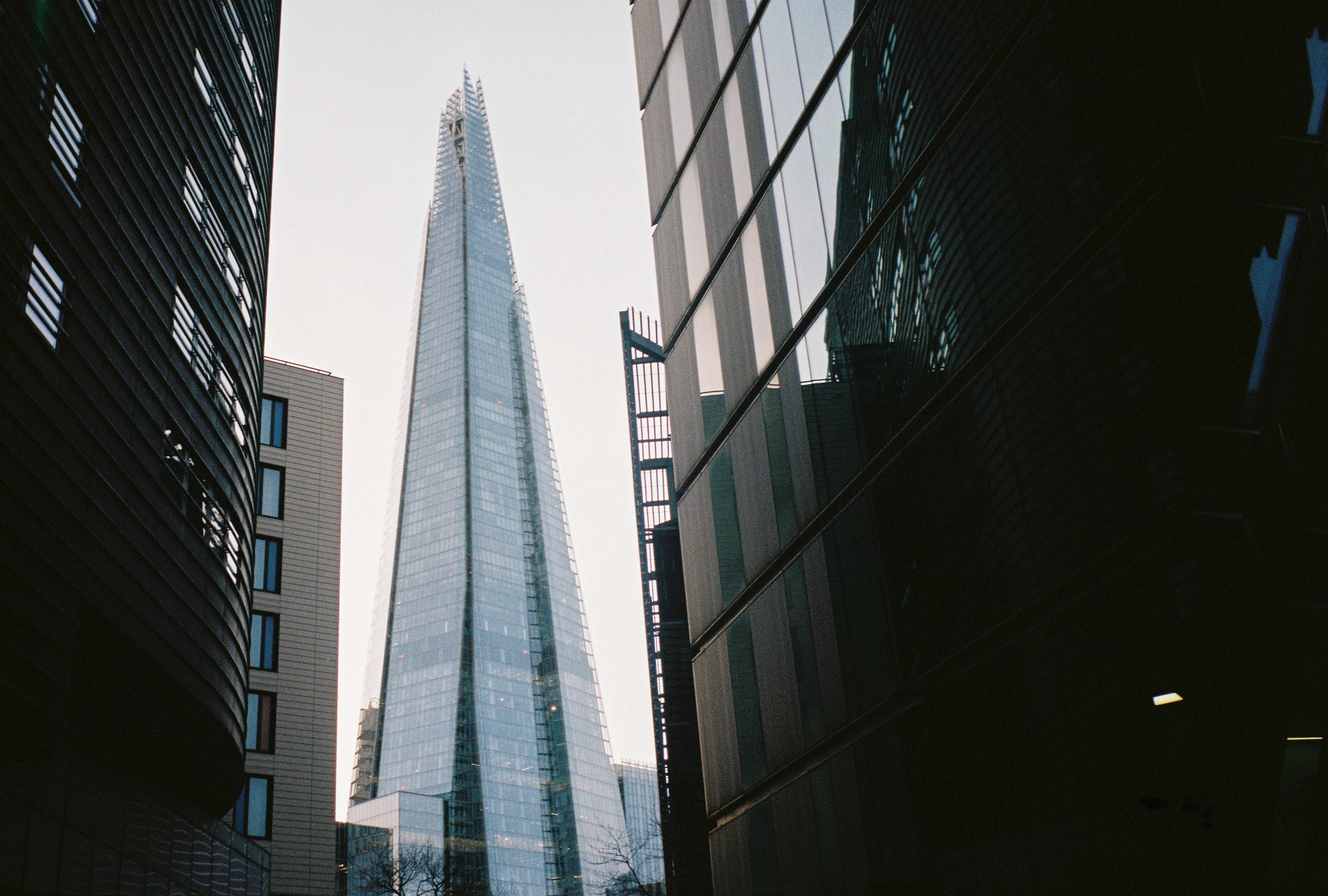 Modern glass skyscraper framed by dark buildings on either side in a cityscape.