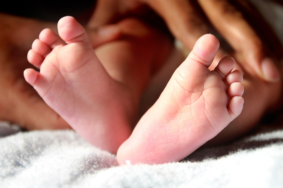 Close-up of a baby's feet resting on a soft white surface with adult hands in the background.