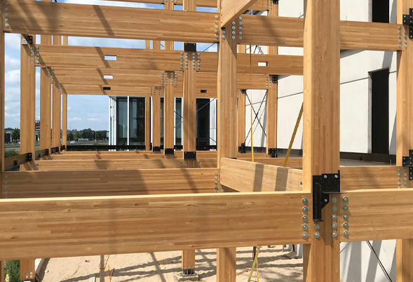 Houten constructie van gelamineerde balken bevestigd met metalen beugels buiten een gebouw onder blauwe lucht.