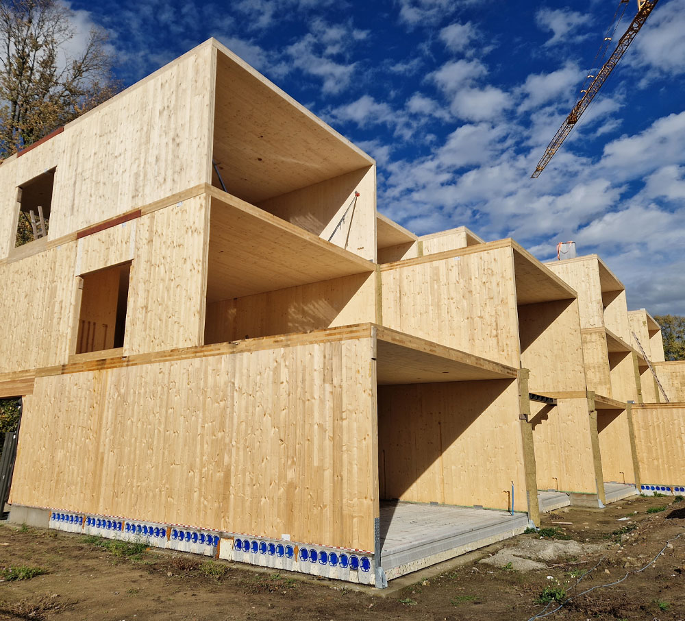 Modulaire houten woning in aanbouw met meerdere verdiepingen onder een partly bewolkte blauwe lucht.