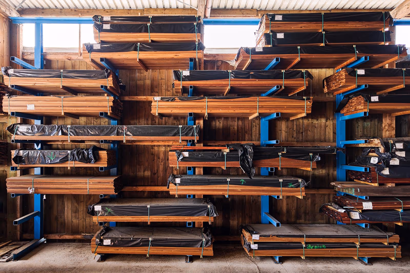 Das Bild zeigt diverses dunkel braunes Holz in einem Regal vor einer Holzwand.