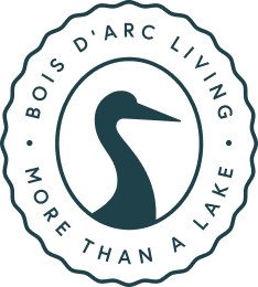 Bois d'Arc Living emblem with heron silhouette surrounded by text 'Bois d'Arc Living' and 'More Than a Lake'.