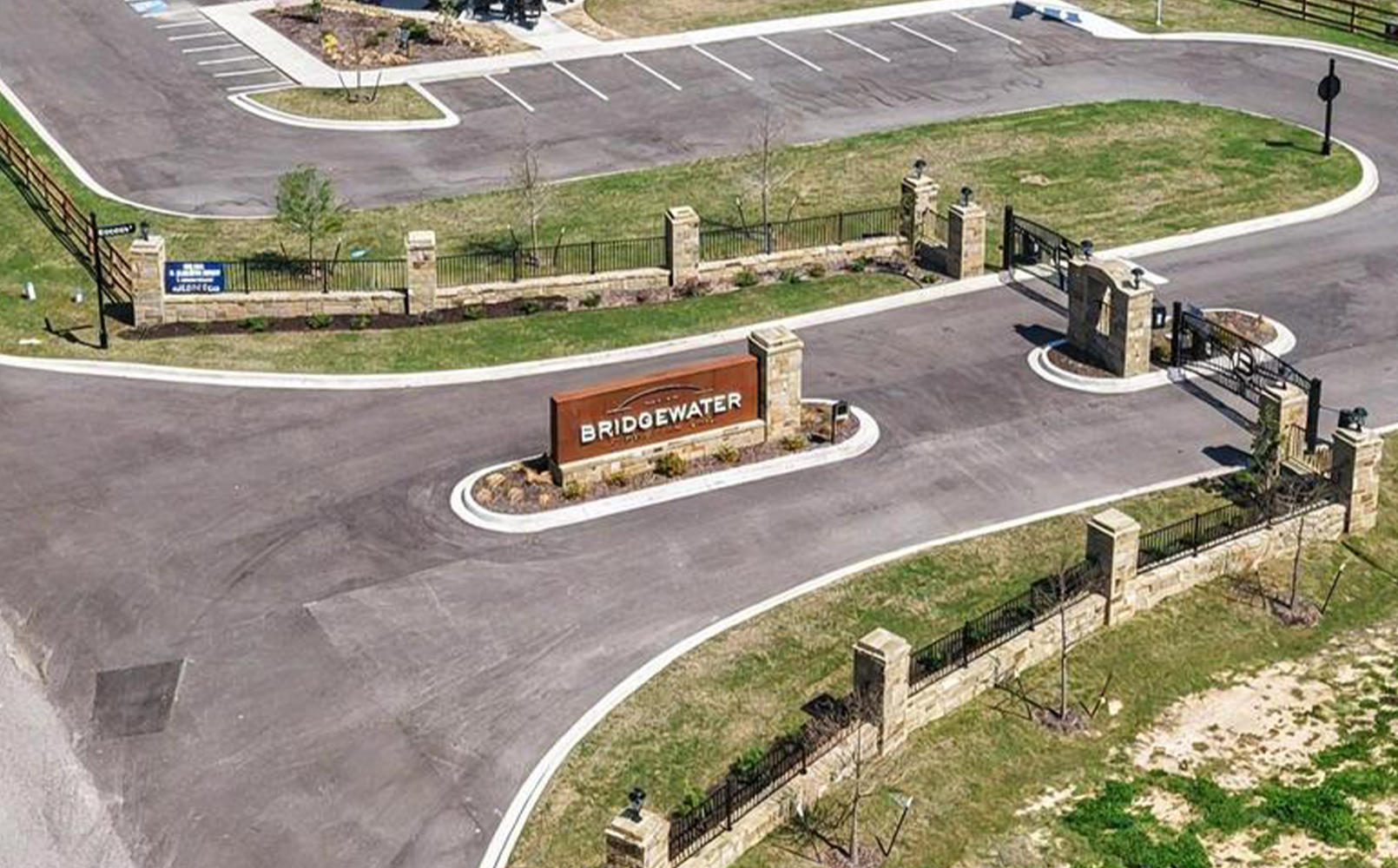 A gated entrance to Bridgewater community with stone pillars, metal fences, and a central welcome sign on a landscaped median.