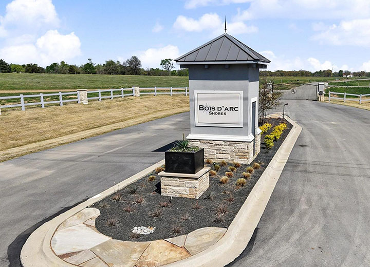 Entrance to Bois D'Arc Shores community marked by a stone and metal sign on a landscaped median with roads on both sides.