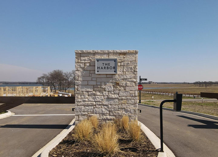 Stone entrance pillar with a sign reading 'The Harbor' at a gated community entrance under a clear blue sky.