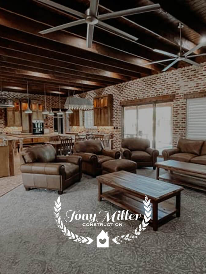 Spacious living room with brown leather sofas, a wooden coffee table, exposed brick walls, and a kitchen with wooden cabinetry and pendant lights in the background.