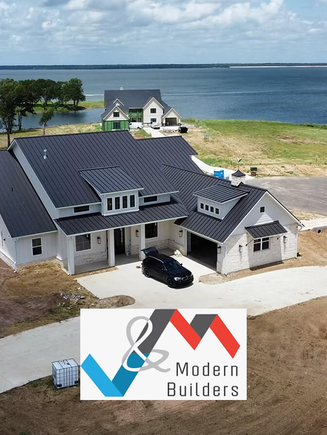 Modern white house with dark metal roof and a black car parked on the driveway, situated near a large body of water with another house visible in the background.