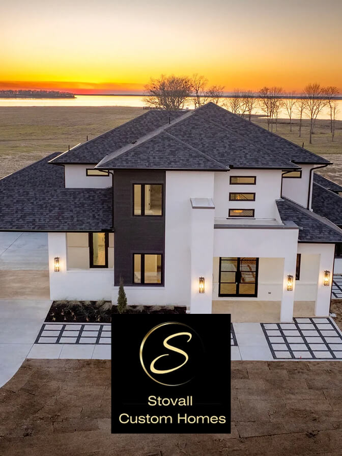 Modern two-story house with dark gray roof and white exterior at sunset, with Stovall Custom Homes logo overlay.