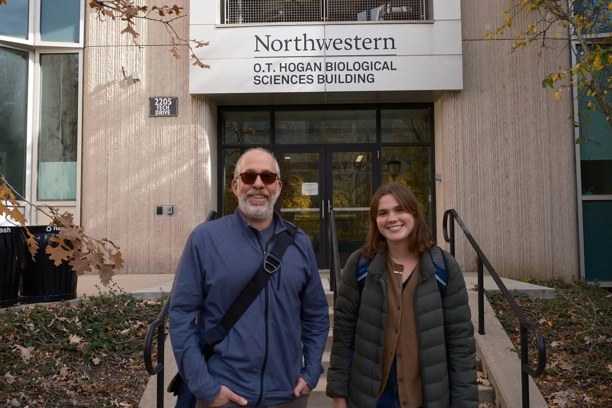 Two people smiling in front of Northwestern's O.T. Hogan Biological Sciences Building entrance.