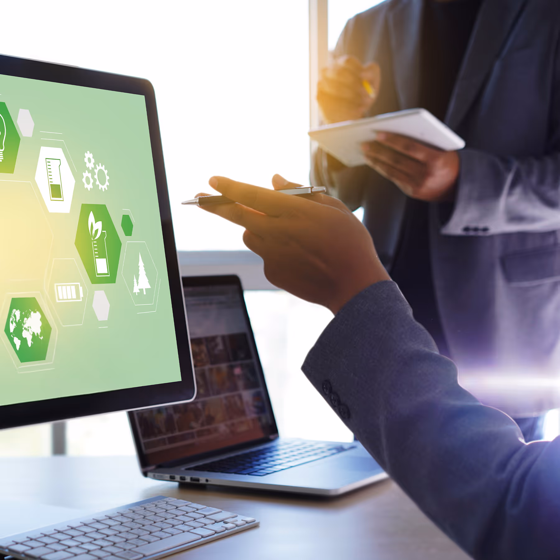 Zwei Personen in Anzügen diskutieren über erneuerbare Energien, angezeigt auf einem Computermonitor mit grünen Symbolen für Umwelt und Nachhaltigkeit.