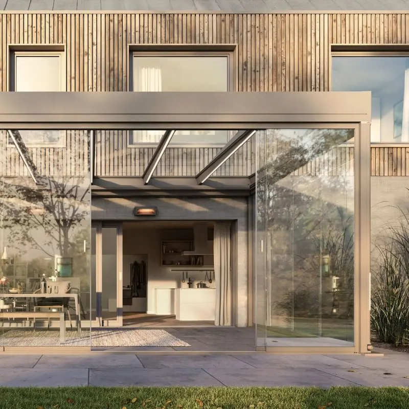 Moderner Wintergarten mit Glas-Schiebetüren und Glasdach an einem Holzhaus mit Blick auf Innenküche und Essbereich.