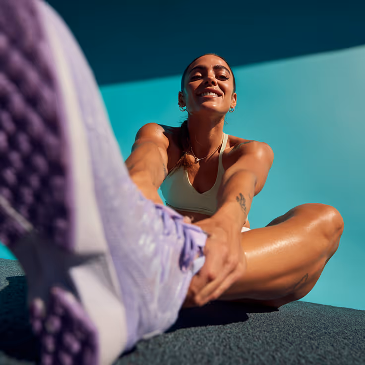 A lady in running clothes, sitting on the floor while smiling