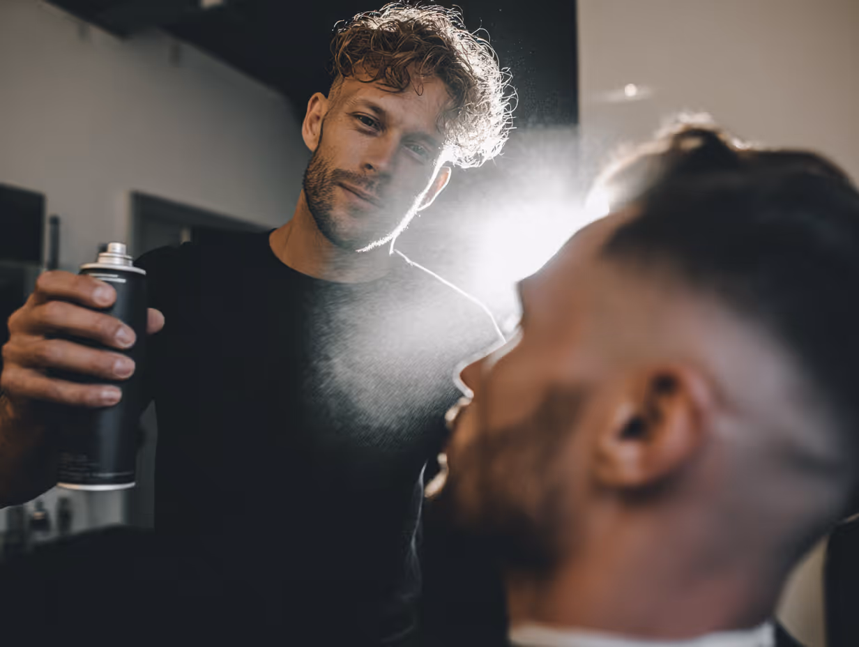 Barber spraying hair product on a client's hair in a salon.