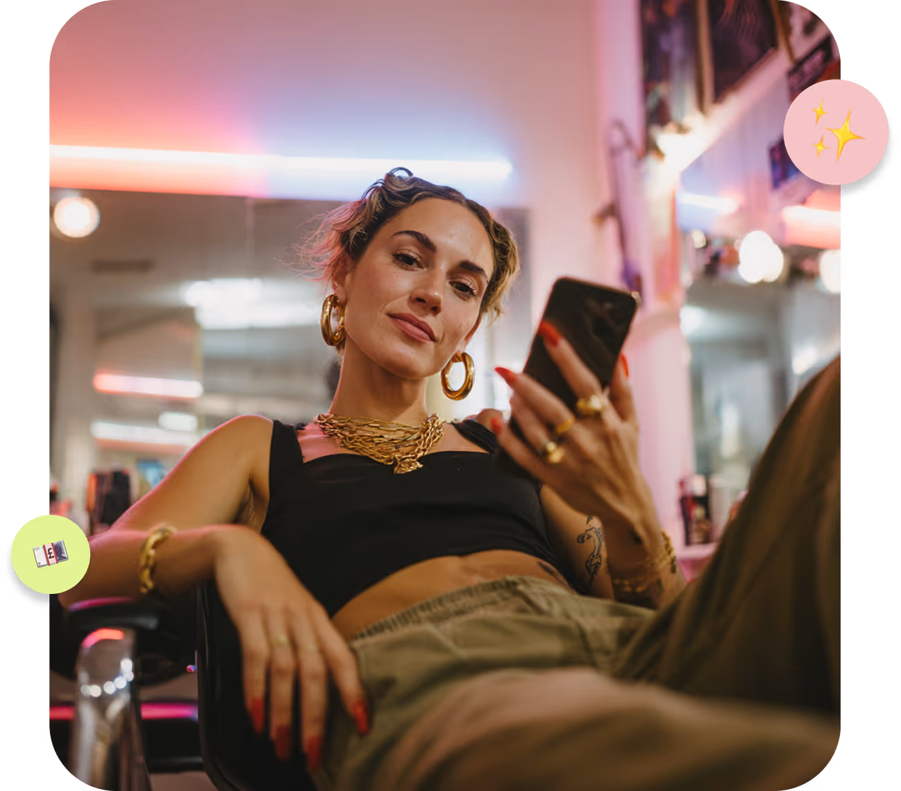 Tattooed woman wearing black gloves performing a facial treatment on a patient lying down with a pink headband and fuzzy sweater in a spa room with pink lighting.