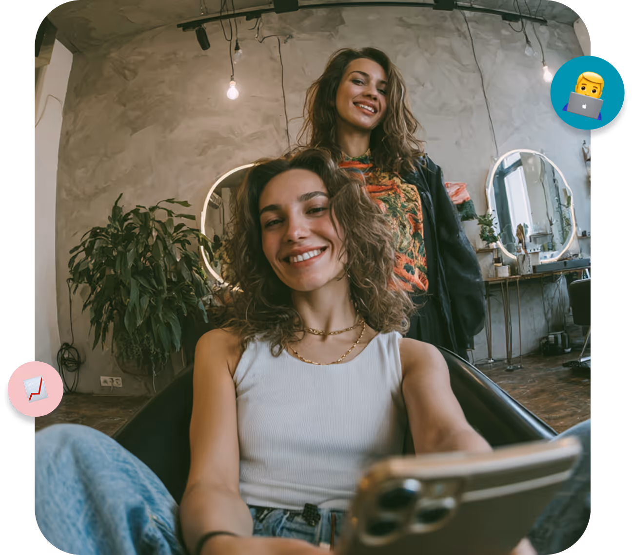Two smiling young women taking a selfie in a stylish salon with round illuminated mirrors and plants.
