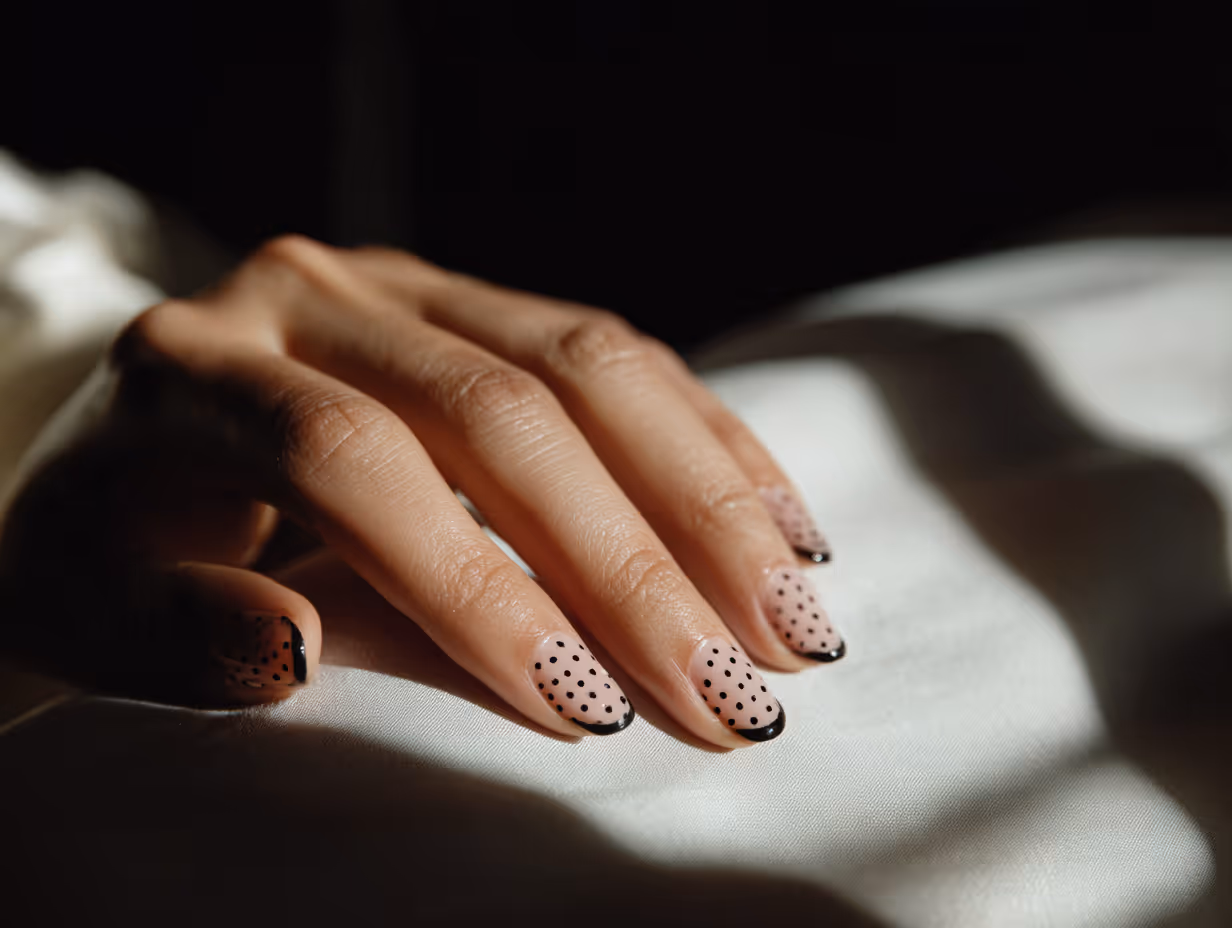 Close-up of lips with glossy maroon lipstick and hands with matching maroon pointed nails touching the chin.