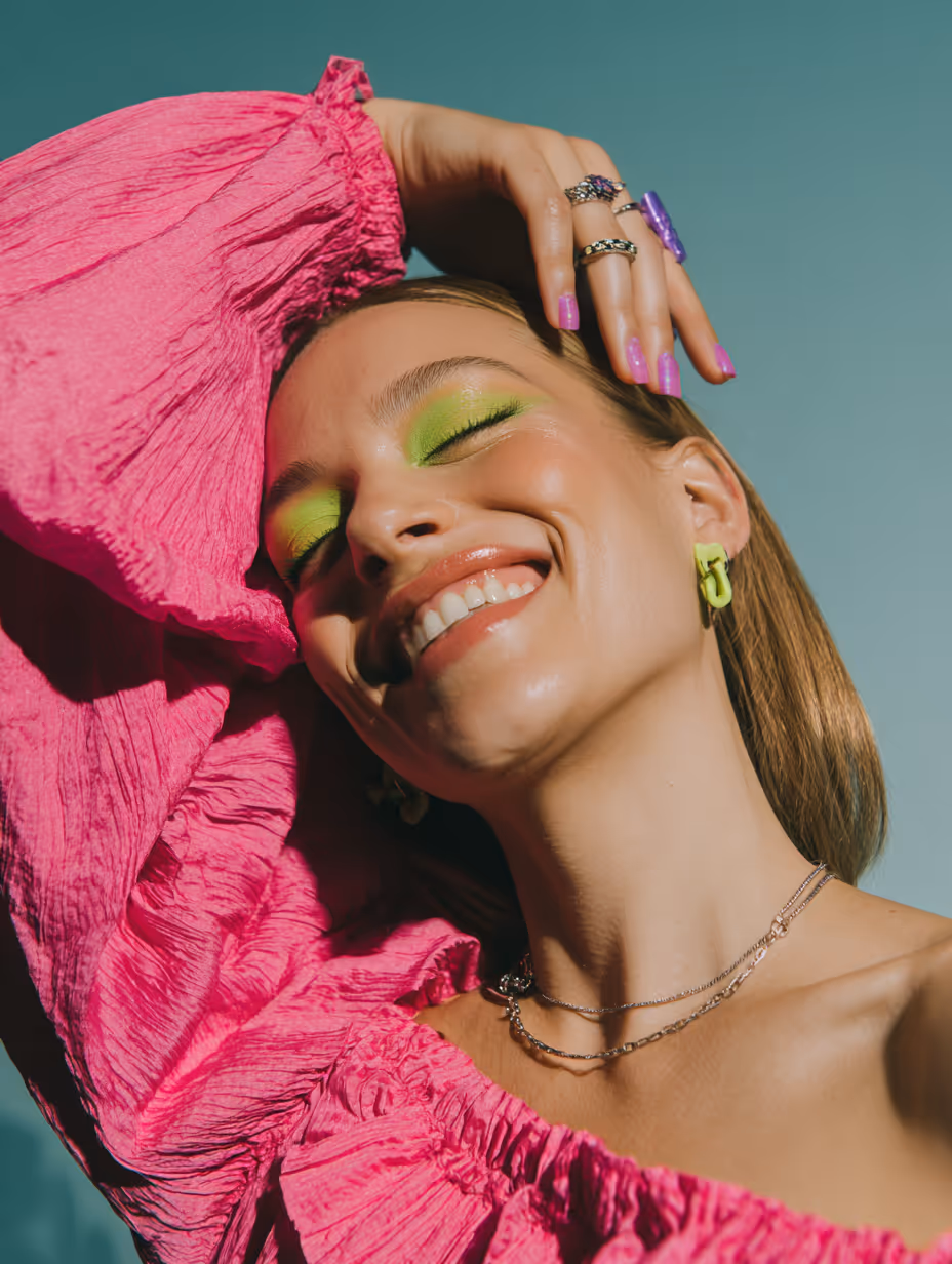 Close-up of lips with glossy maroon lipstick and hands with matching maroon pointed nails touching the chin.