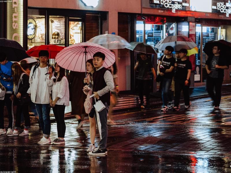 Varias personas paseando por un barrio de Seúl en una noche lluviosa.