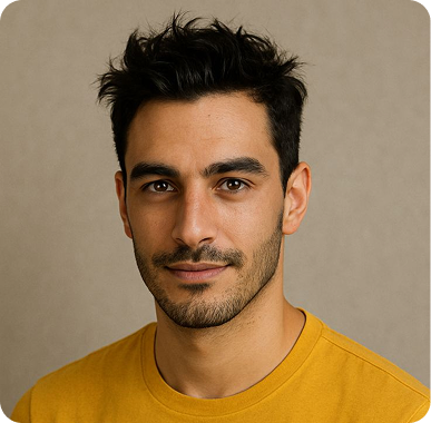 Portrait of a man with short black hair and facial hair wearing a mustard yellow shirt against a beige background.