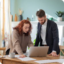 Two colleagues, a woman and a man, reviewing documents together at a desk with a laptop in a modern office.