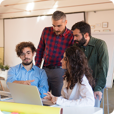 Four colleagues gathered around a laptop, engaged in a discussion in a bright office.