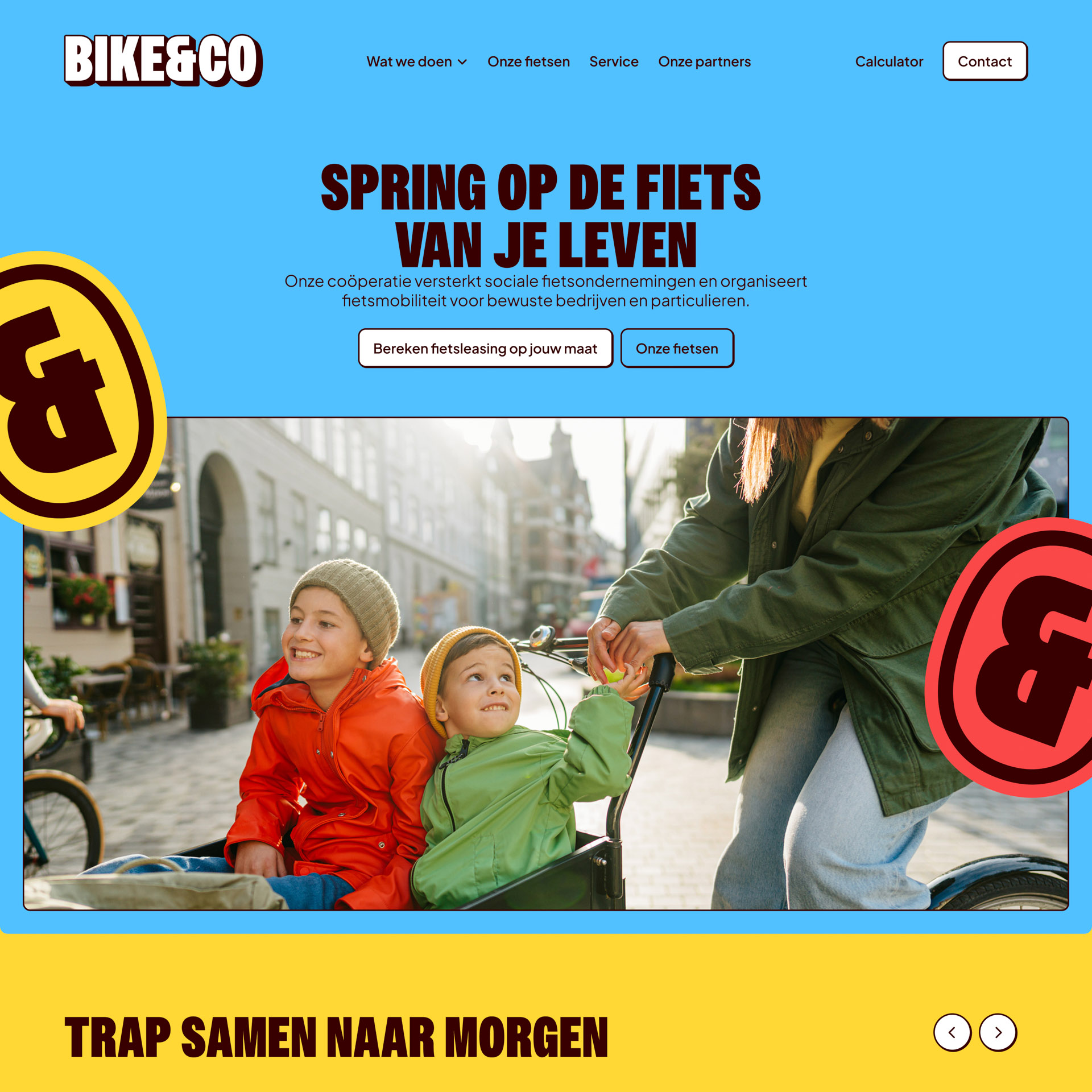 Twee kinderen in felgekleurde jassen in een bakfiets terwijl een volwassene hen voortduwt op een zonnige straat in de stad.