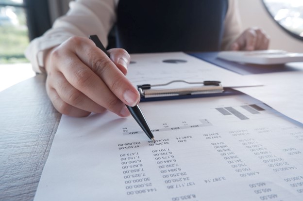 Close-up of a person auditing financial data on printed invoice documents.