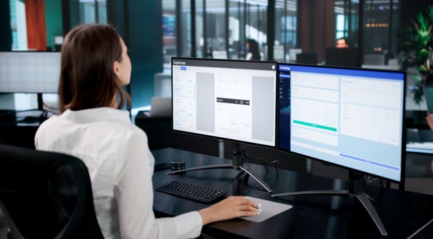 Employee reviewing automated invoicing and expense dashboards across dual monitors.