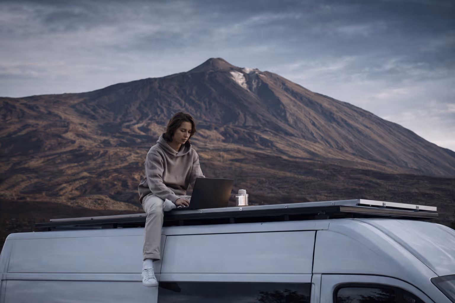 Person sitting on campervan roof with mountain landscape view