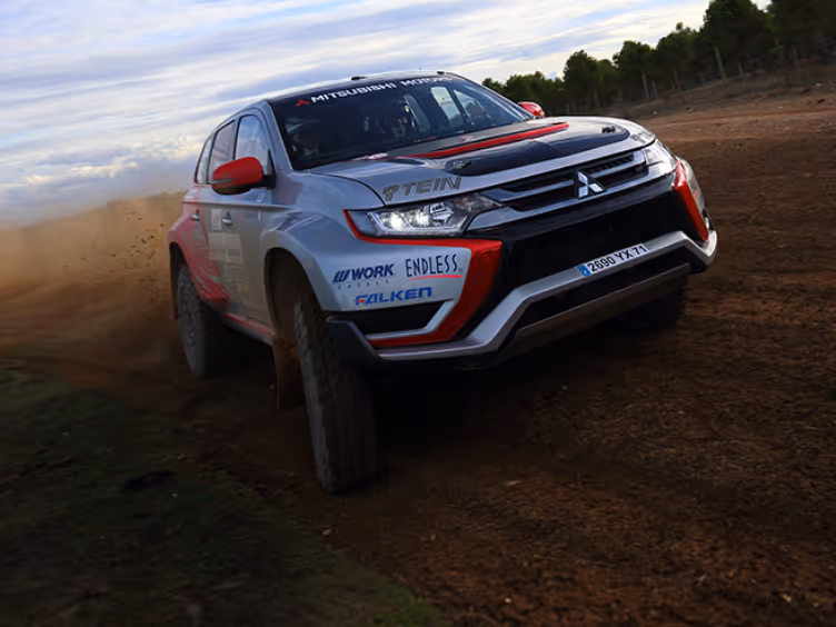 Four Mitsubishi SUVs parked on grass with large trees in the background, featuring blue, white, red, and white models.