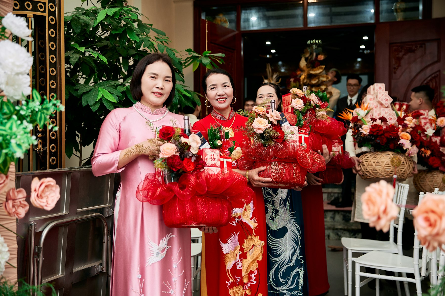 Women in áo dài carrying red gift baskets at a Vietnamese wedding