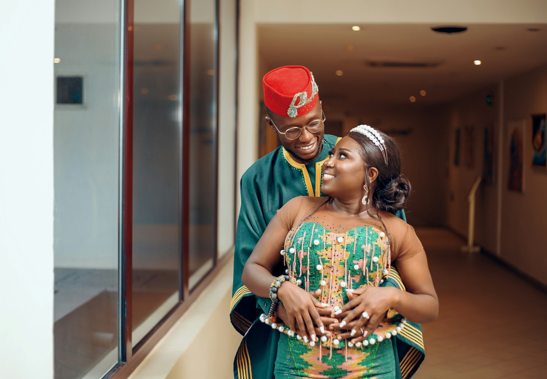 A smiling bride in a beaded kente gown embraced by her groom in green and gold at their wedding in Ghana