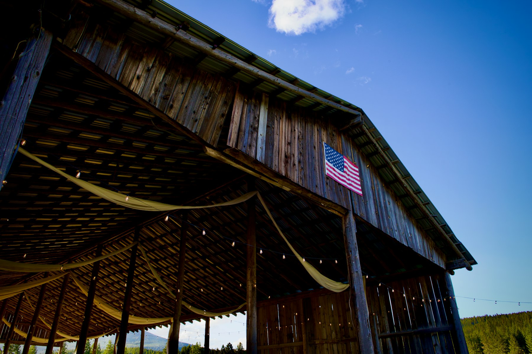 Eine rustikale Holzscheune als Hochzeitslocation mit amerikanischer Flagge, drapiertem Stoff und Lichterketten