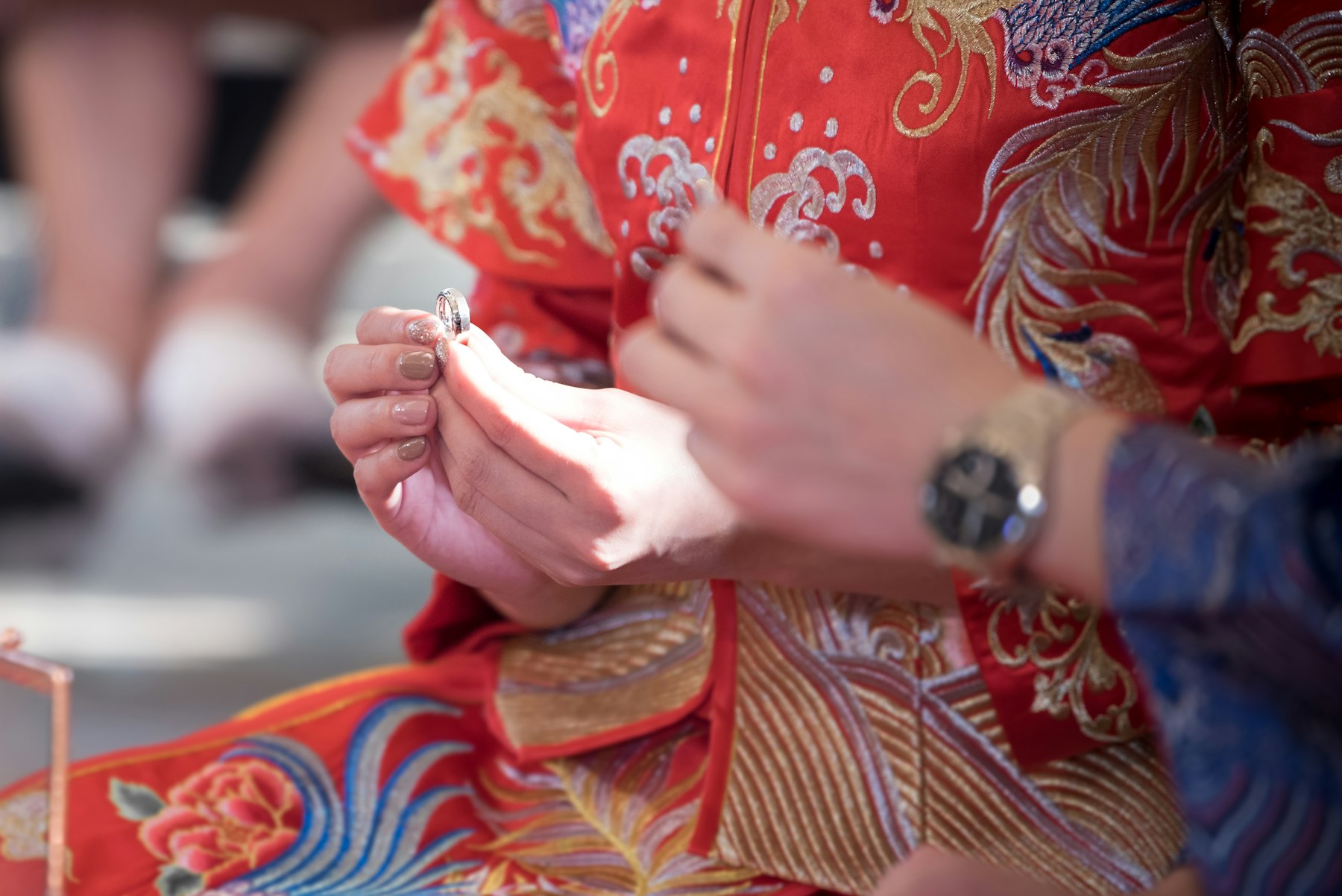 Close-up of a bride in an embroidered red qun gua receiving her wedding ring