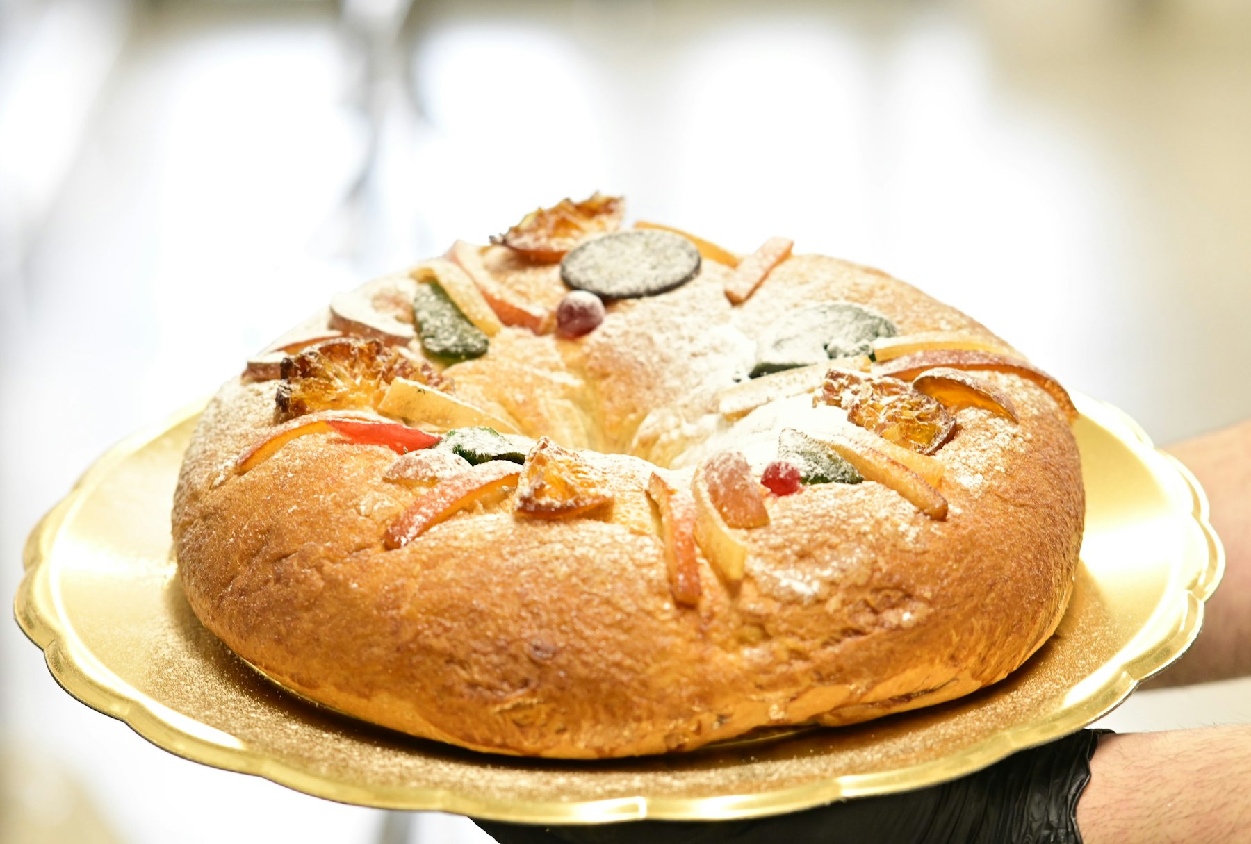 Ein Roscón de Reyes, ein Hefekranz mit kandierten Früchten und Puderzucker, auf einem goldenen Tablett