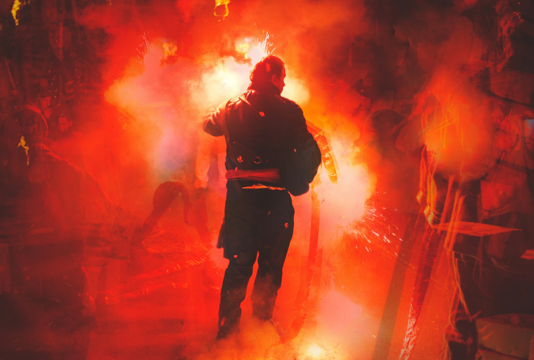 Double exposure of a figure walking through red flare smoke and sparks at Lewes Bonfire Night in East Sussex