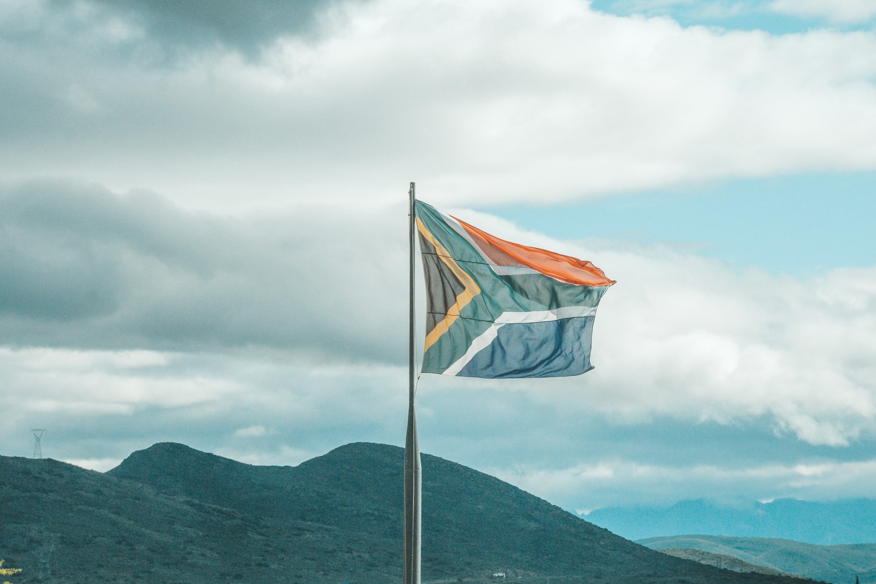 The South African flag flying high above green hills under a cloudy sky