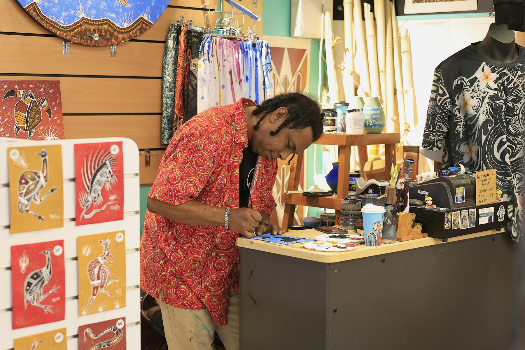 An artist painting in traditional Aboriginal style at his stall in Cairns, surrounded by his artworks