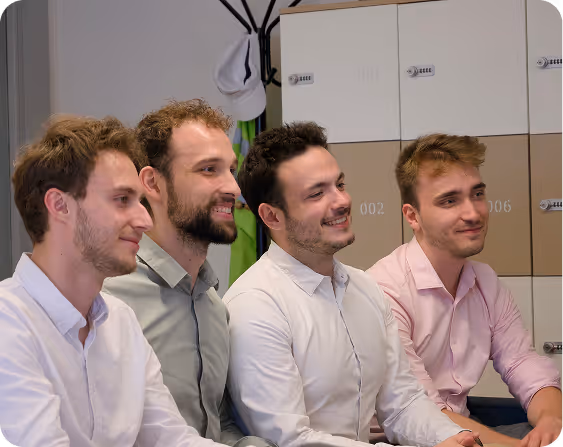 Four smiling Pixacare team members, dressed in shirts, in an office with lockers in the background.