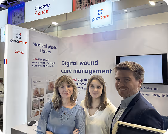 Three Pixacare team members stand in front of a Pixacare exhibition booth about digital wound management and the medical photo library.