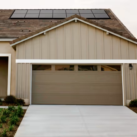 Beige house with a closed garage door and solar panels installed on the roof.