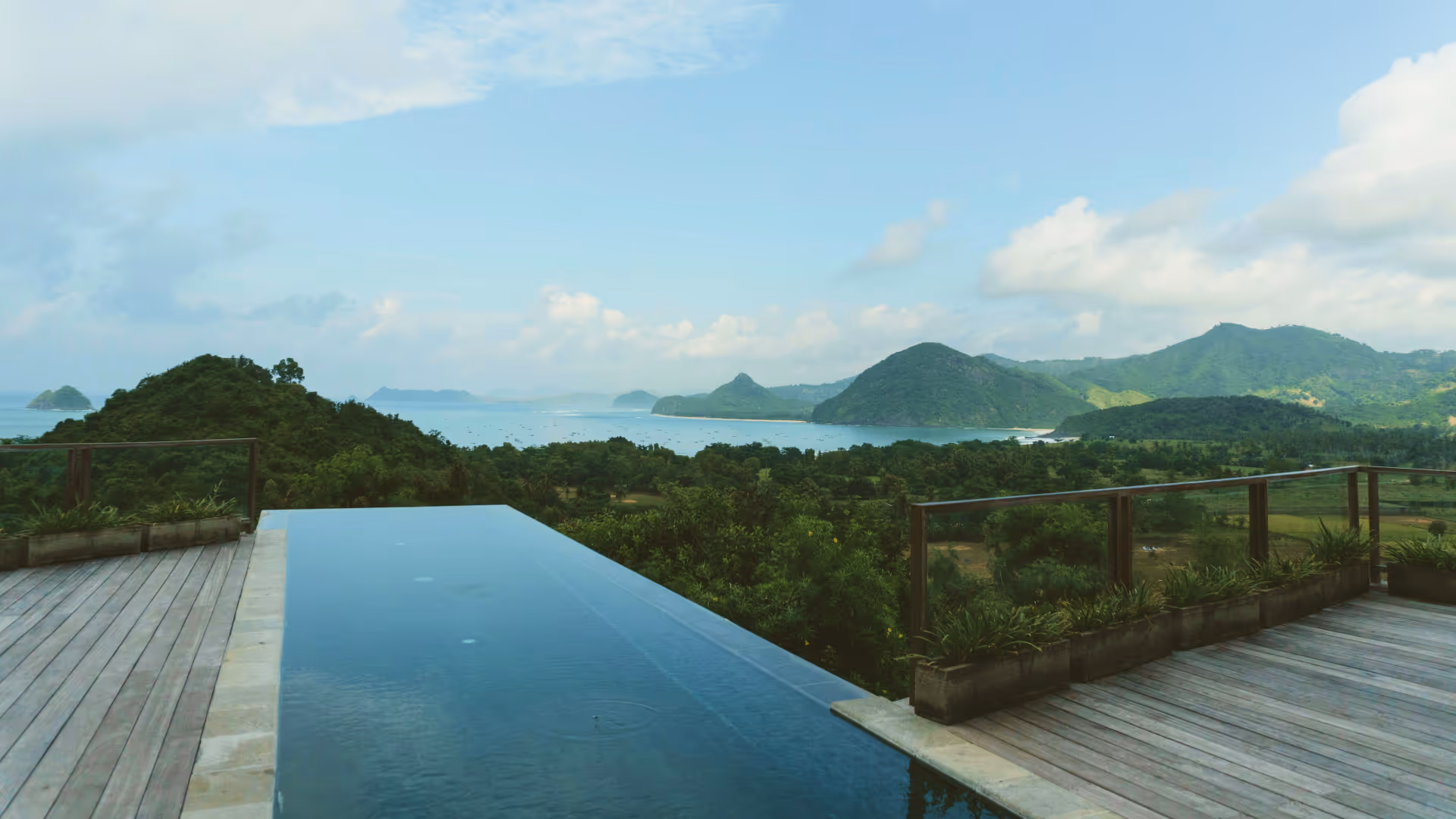 Infinity pool overlooking lush greenery and hills under a partly cloudy sky.