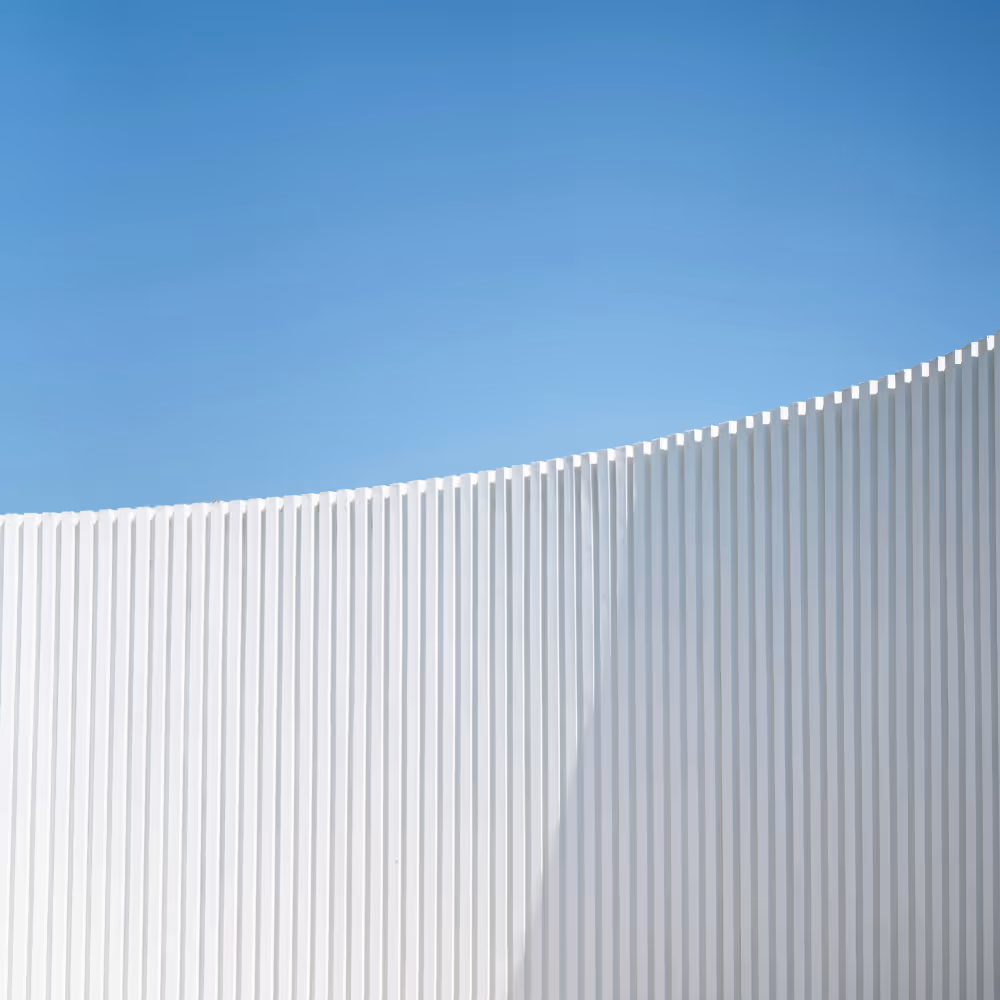 Curved white ribbed wall under clear blue sky casting a shadow.