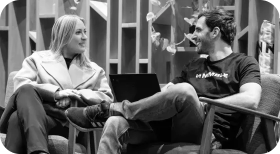 Man and woman sitting in chairs facing each other, engaged in conversation with a laptop on the man's lap.
